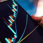 Hand holding tablet showing stock market candlestick chart.