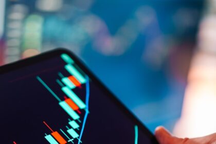 Hand holding tablet showing stock market candlestick chart.