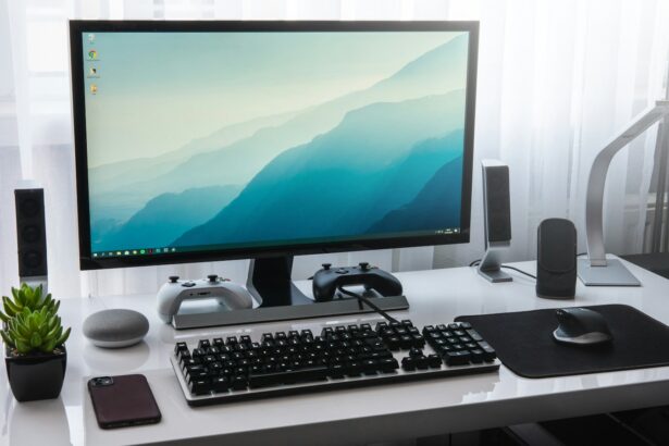 A computer monitor, keyboard, and game controllers on a white desk in a workspace