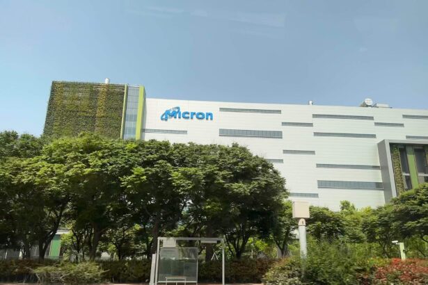 White Micron fab building with the Micron logo, behind a row of trees and a bus stop in Taichung, Taiwan