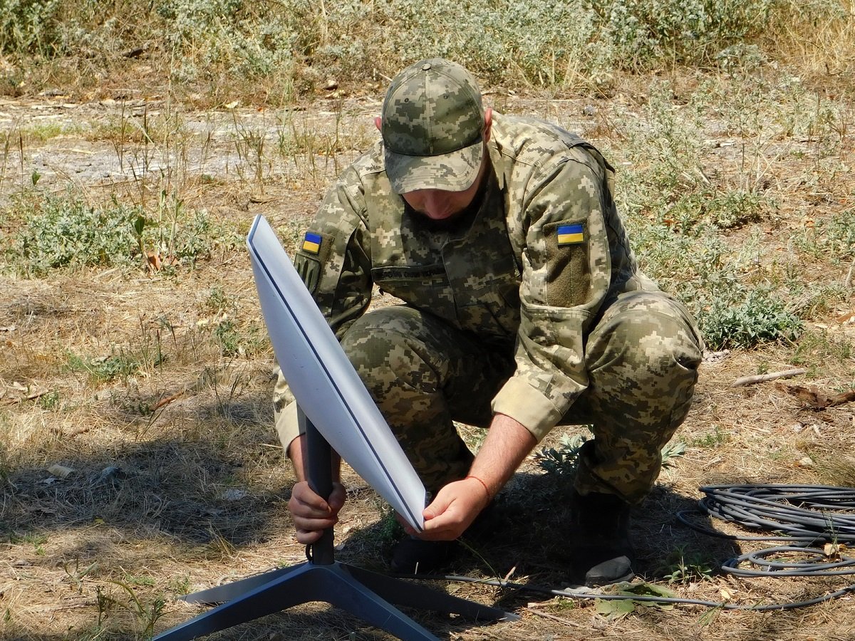 A Ukrainian soldier setting up a Starlink satellite terminal in a field